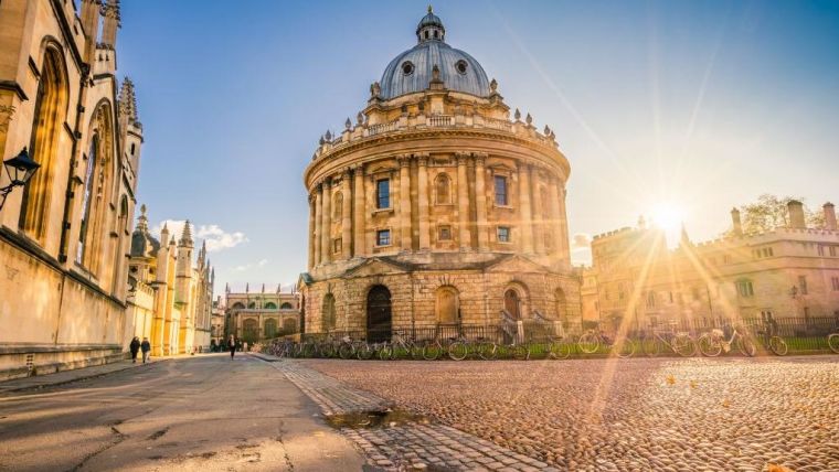 Sunlit street view of the Radcliffe Camera, Oxford, with bikes around the metal railings outside the building