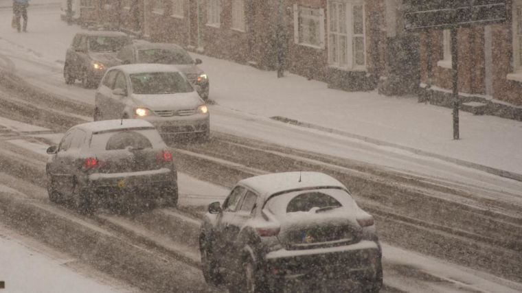 Cars driving in blizzard conditions down a typical UK street.