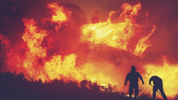 Two firefighters silhouetted against a wildfire