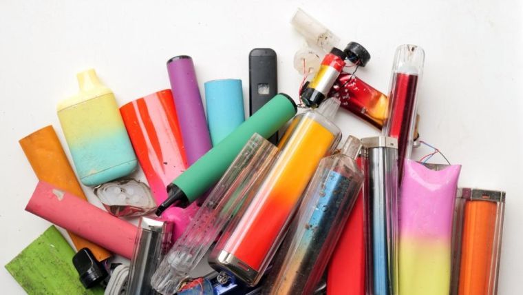 A brightly-coloured collection of discarded electronic cigarette vapes and internal components shot over a white plastic background.