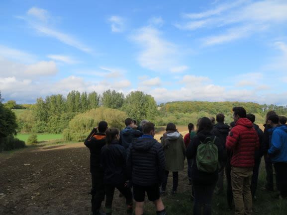 Students overlooking the Evenlode river across a ploughed field